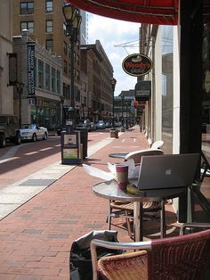 an open laptop computer sitting on top of a wooden table next to a street filled with parked cars