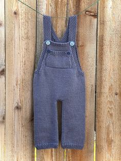 a pair of blue knitted overalls hanging on a wooden fence