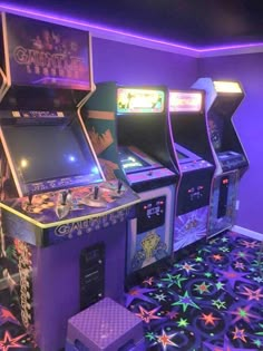 three arcade machines in a room with purple walls and stars on the floor next to them