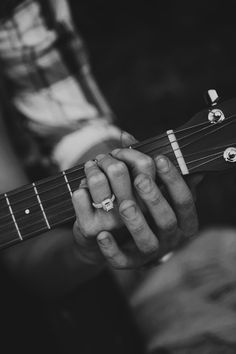 a person playing an acoustic guitar with their hands and fingers holding the strings, black and white photo