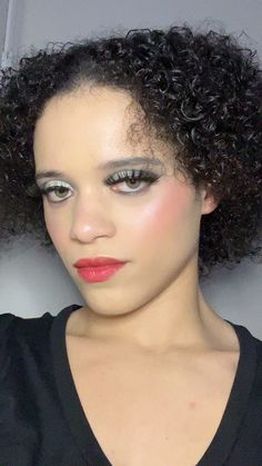 a woman with curly hair and blue eyeshadow is posing for the camera while wearing red lipstick