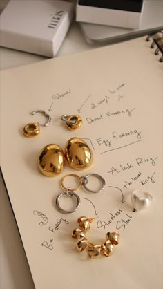 five pairs of earrings sitting on top of a piece of paper next to a pen