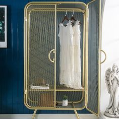 a white dress is hanging on a rack in a room with blue walls and an angel statue