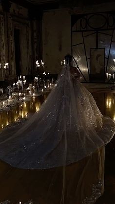 the bride is wearing a long veil and standing in front of rows of lit candles