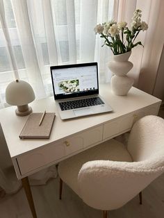 a laptop computer sitting on top of a white desk next to a vase with flowers