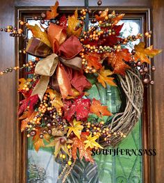 a wreath with autumn leaves and berries hanging on a door