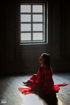 a woman sitting on the floor in front of a window wearing a red kimono