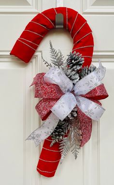 a red wreath with pine cones and white ribbon hanging on a front door decorated for christmas