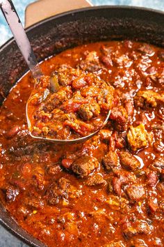 a spoon full of chili and meat in a skillet on a blue counter top