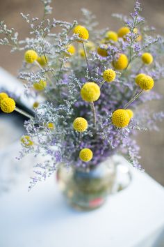 a vase filled with lots of yellow flowers on top of a table next to a window