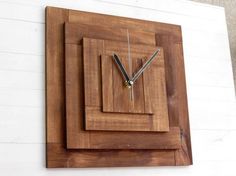 a square wooden clock mounted to the side of a white wall with two black hands