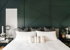 a bed with white sheets and pillows in a room that has dark green paint on the walls