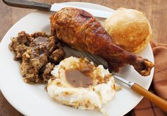 a white plate topped with meat, potatoes and gravy next to a roll