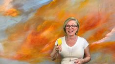 a woman holding a yellow object in front of a colorful painting with clouds and sky