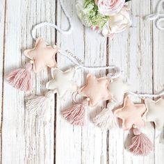 some pink and white stars hanging on a string with tassels next to flowers