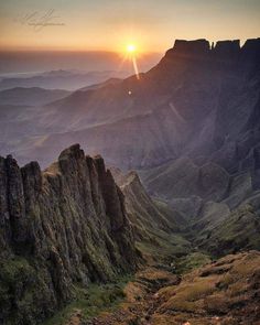 the sun is setting over some mountains in the distance, with grass growing on the ground