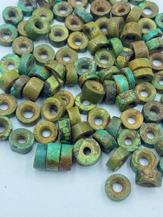 several pieces of green and gold colored beads on a white surface with holes in the middle