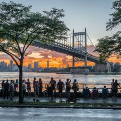 a group of people standing next to each other on a sidewalk near the water with a bridge in the background