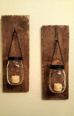 two mason jars are hanging on the wall with chains attached to them, and one has a candle in it