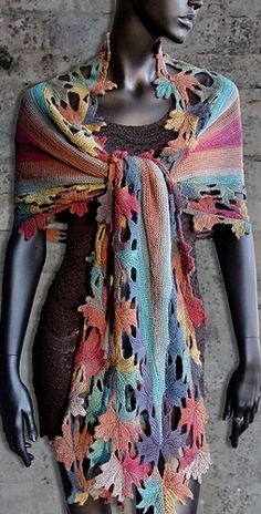 a mannequin wearing a multicolored shawl in front of colorful leaves