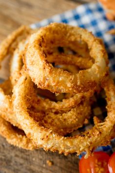 fried onion rings are stacked on top of each other with cherry tomatoes in the background