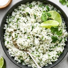 a bowl filled with rice, cilantro and limes next to sliced limes