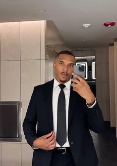 a man in a suit is taking a selfie with his cell phone while wearing a black tie