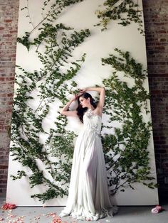 a woman in a white dress standing next to a wall with ivys on it