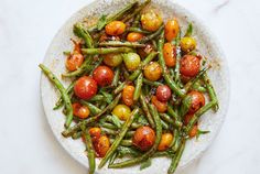 a white plate filled with green beans and tomatoes on top of a marble countertop