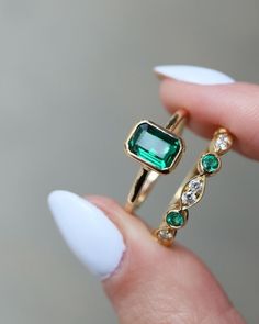 a woman's hand holding a ring with an emerald and diamond set in it