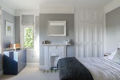 a bedroom with gray walls and white bedding has a fireplace in the corner next to it