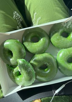 a box filled with green donuts sitting on top of a table next to pillows