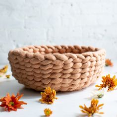 a woven bowl with flowers on the side and white brick wall in the back ground