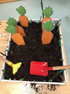 the garden is made out of dirt and plastic carrots with gardening utensils