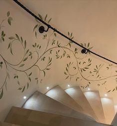 the stairs are decorated with green leaves and vines on white painted walls, along with black metal handrails