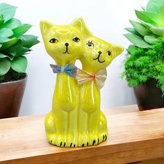 a yellow cat figurine sitting on top of a wooden table next to potted plants