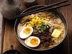 a bowl of ramen with eggs, meat and vegetables on a wooden table next to chopsticks