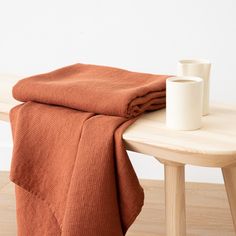 a wooden table topped with a white cup and orange blanket next to a wood bench