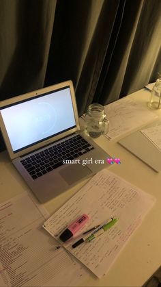 an open laptop computer sitting on top of a white desk next to papers and pens