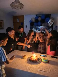 a group of people standing around a table with a birthday cake on top of it