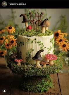 a cake decorated with mushrooms and plants on top of a wooden table next to sunflowers