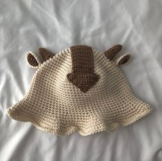 a crocheted hat is laying on top of a white sheet with a brown teddy bear