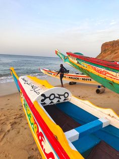 several colorful boats are on the beach near the water's edge and one person is standing next to them