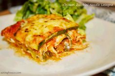 a white plate topped with lasagna covered in cheese and sauce next to a green salad