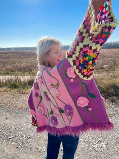 a woman in a pink sweater is holding up a colorful scarf