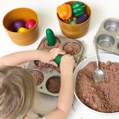 a child is playing with chocolate in a muffin pan