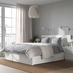 a white bed sitting next to a window in a room with wooden flooring and furniture