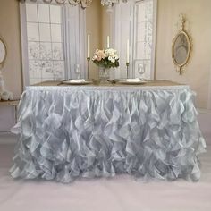 a table covered in ruffled cloth with candles and flowers on the table next to it