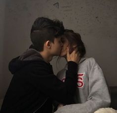 two people kissing each other in front of a wall