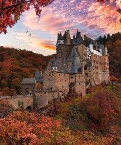 an old castle sits on top of a hill surrounded by trees and leaves in the fall